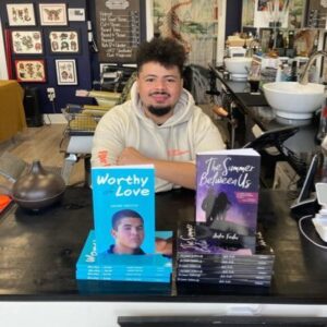 A young person sits smiling behind two of his novels.